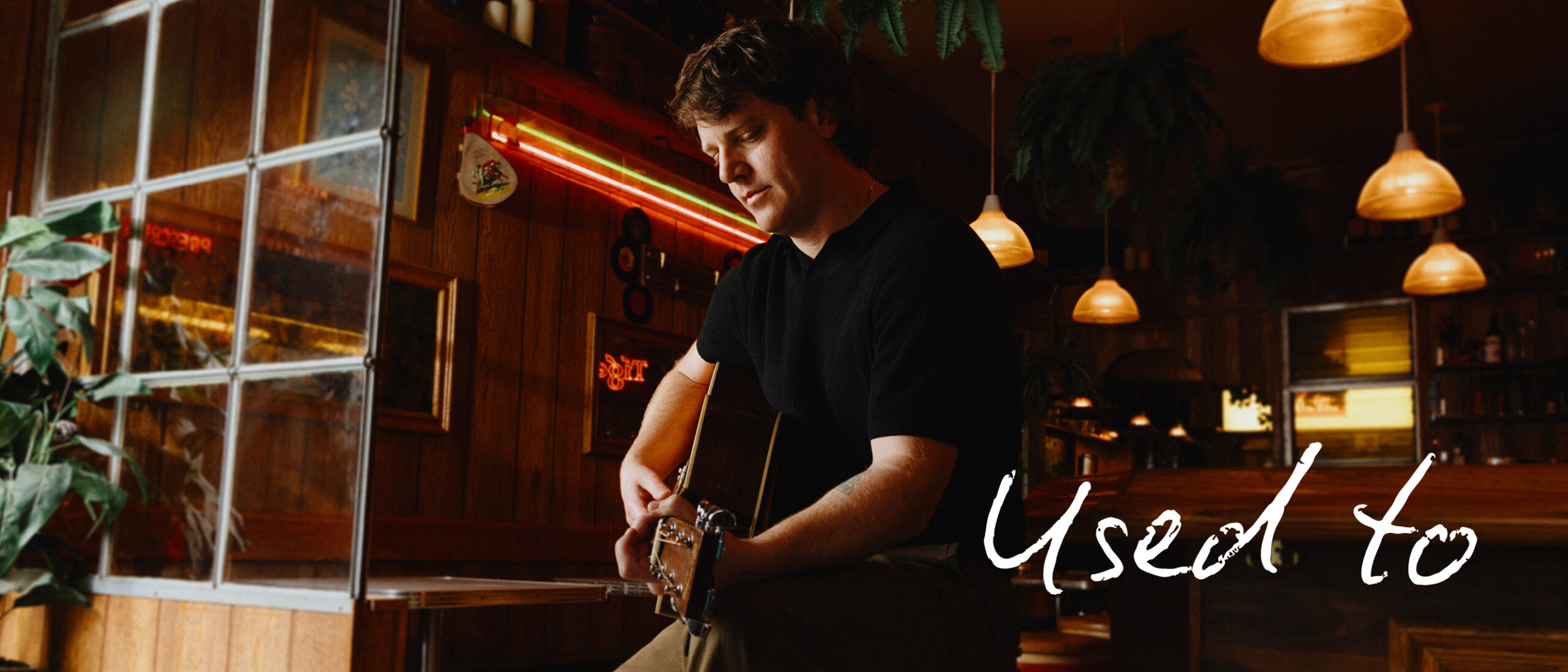 a handsome middle aged man sitting down in a Toronto bar playing an acoustic guitar